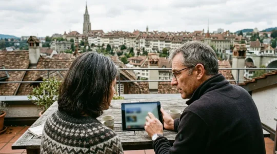 Un couple d'une cinquantaine d'années consulte une tablette sur leur terrasse, regard concentré vers l'écran, toits de ville en arrière-plan